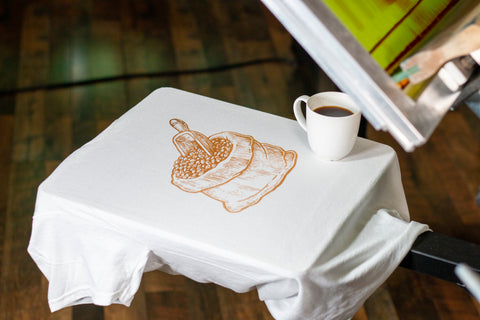 Kantong bubuk kopi dengan sablon di atas T-shirt putih dengan secangkir kopi 